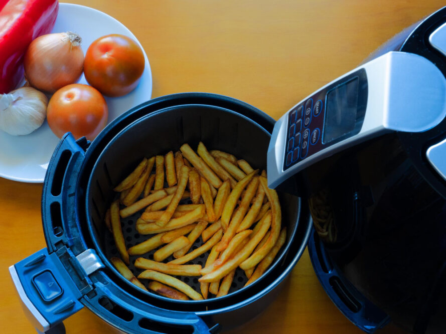 Ansicht von oben auf eine Heißluftfritteuse auf einem Tisch mit Pommes Frites und Gemüse - gesundes Essen Konzept als Symbolbild für den Ratgeber: Worauf muss ich beim Kauf einer Heißluftfritteuse achten?