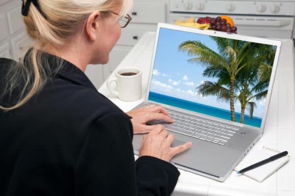 Büroangestellte blickt auf einen Bildschirm mit Strand und Palmen im Hintergrund - Symbolfoto Urlaub zu Ende, wieder arbeiten