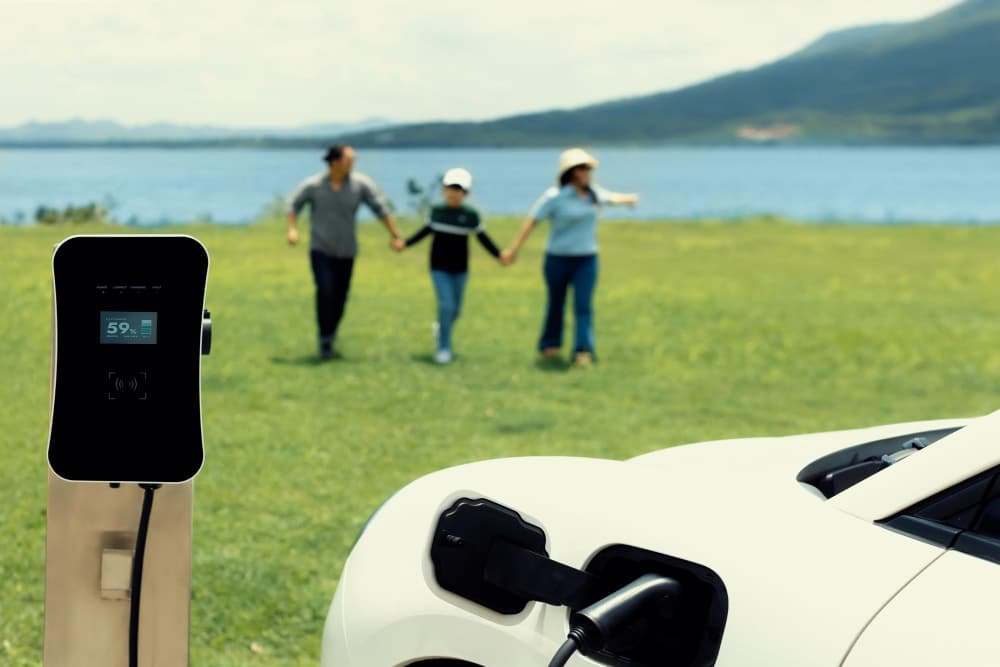 Familie im Urlaub mit dem Elektroauto, welches gerade an einer Wallbox lädt