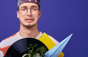 Junger Mann der die Miene verzieht und einer Schallplatte im Karton vor sich als Symbolbild für den Ratgeber: Ohrwurm loswerden