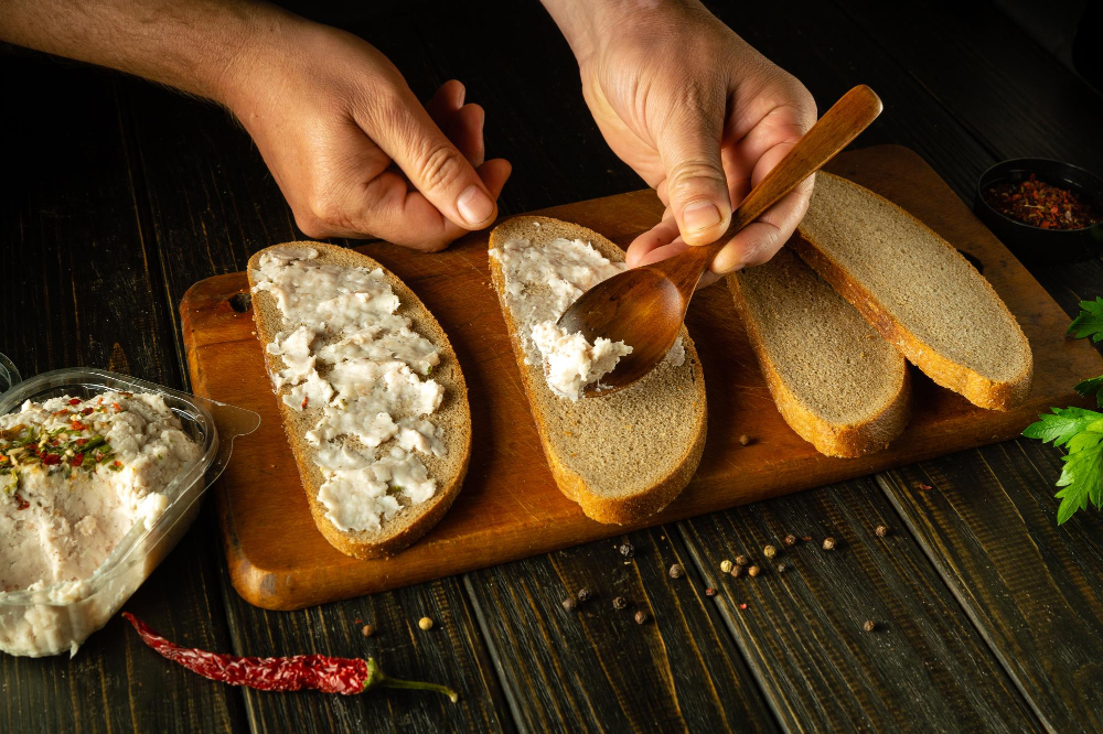 Ein Holzlöffel in den Händen eines Kochs, mit dem er geriebenes Schmalz auf Roggenbrot streicht, um herzhafte Sandwiches für eine Brotzeit zuzubereiten als Symbolbild für den Ratgeber: Alternativen zu Schmalz