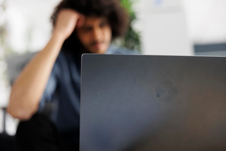 Verzweifelte junger Mann im Hintergrund am Laptop als Symbolbild für den Ratgeber: Wie lange bekommt man Halbwaisenrente?