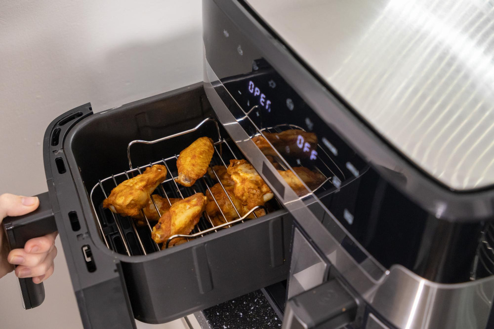 Jemand öffnet eine Heissluftfritteuse oder einen Airfryer mit fertigem Frittiergut.