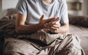 Mann sitzt im Bett und massiert seine taube Hand, weil ihm nachts die Arme eingeschlafen sind.