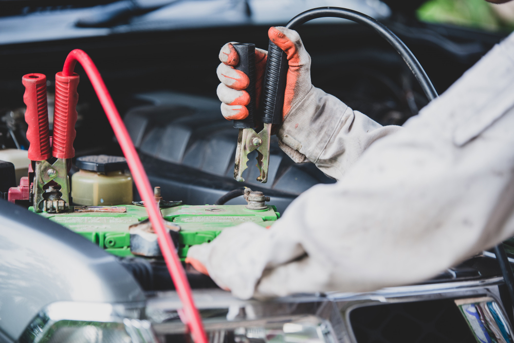 Eine Person hält ein Überbrückungskabel, das an eine Autobatterie angeschlossen ist, um diese aufzuladen. Das Bild zeigt den Prozess des Aufladens einer Autobatterie, ein häufiger Vorgang bei leerer Batterie.