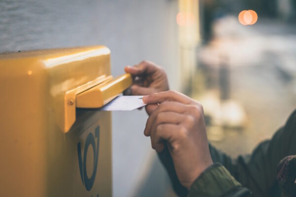 Person steckt einen korrekt beschrifteten Brief in den gelben Postbriefkasten