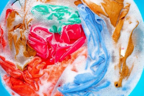 Bunte Kleidung in Seifenlauge, rot, blau, orange und grün vermischt in einem Wasserbehälter.
