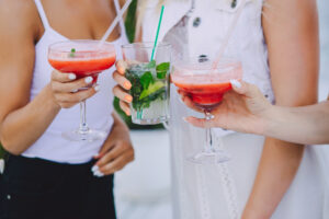 Drei Frauen stoßen mit bunten Cocktails in Sommerkleidung an