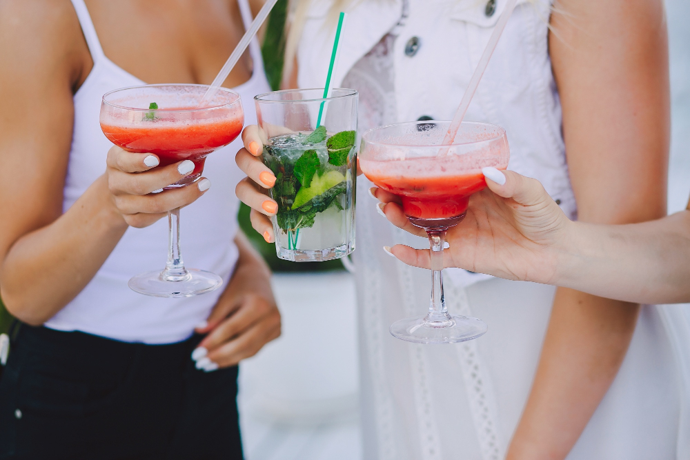 Drei Frauen stoßen mit bunten Cocktails in Sommerkleidung an