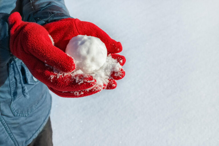 Person mit roten Handschuhen hält einen Schneeball, passend zur Frage „Darf man Passanten mit Schneebällen bewerfen?“