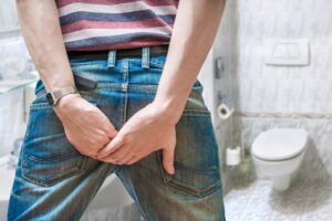 Ein Mann der sich mit beiden Händen den Poppes hält vor einer Toilette als Symbolbild für den Beitrag: Synonyme für kacken