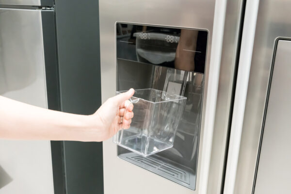 Frau hält Behälter aus Kunststoff unter den Eiswürfelbereiter eines Side by Side Kühlschrank und es kommt nichts