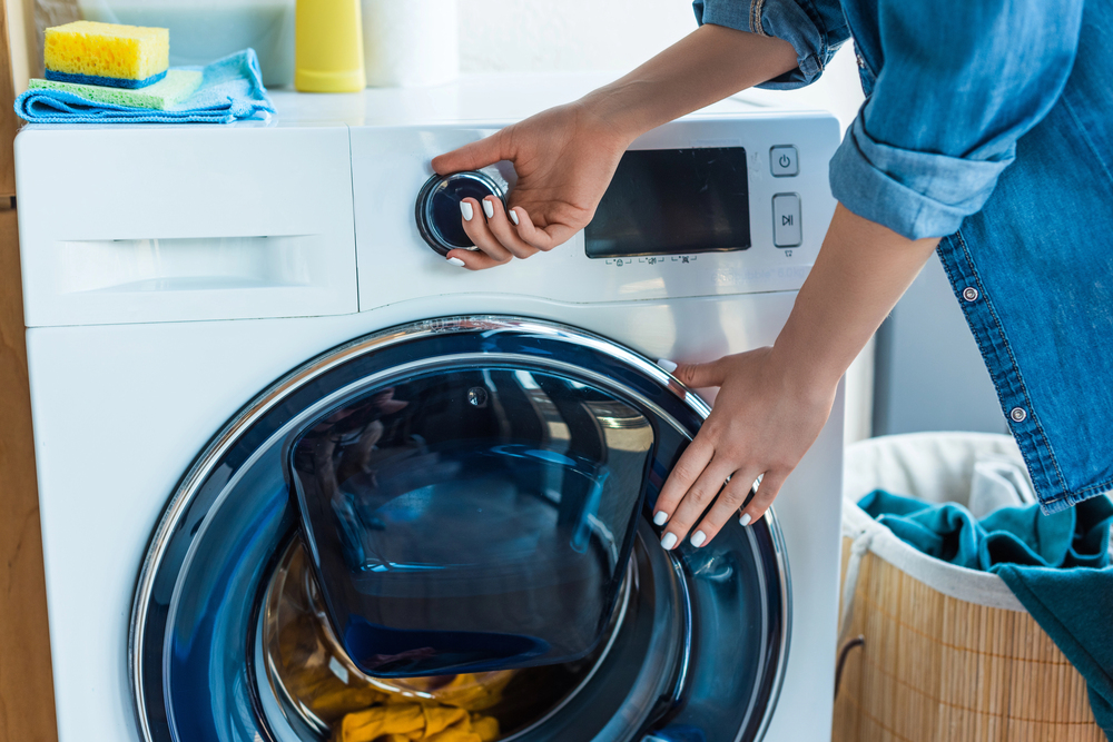 Frau steht an der Waschmaschine, hält die Tür und dreht am Knopf als Symbolbild für den Ratgeber: Waschmaschine schleudert nicht