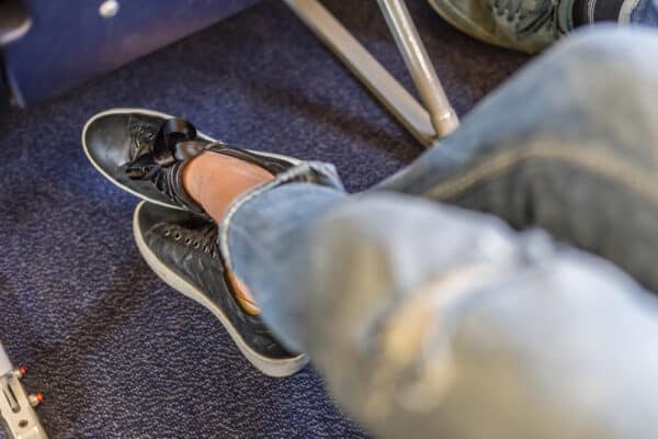 Sitzende Person im Flugzeug Blick auf die Füße als Symbolbild für den Ratgeber: Dicke Knöchel nach dem Fliegen