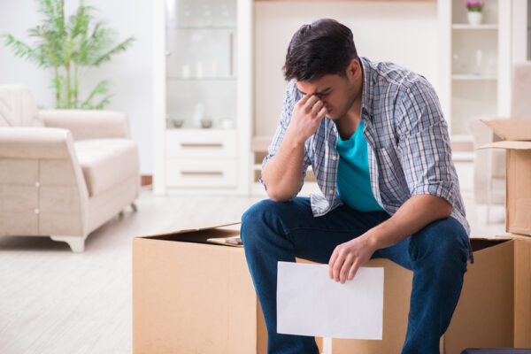 Verwzeifelter junger Mann sitzt auf Umzugskartons mit einem Brief in der Hand als Symbolbild für den Ratgeber: Kündigung wegen Eigenbedarf Mieter findet keine Wohnung