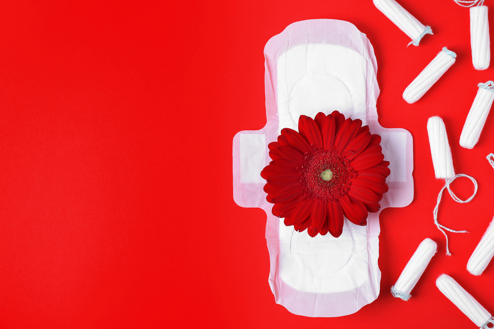 Hygieneartikel für die Periode mit einer roten Blume als Symbolbild für den Ratgeber: Mit Periode zum Frauenarzt?