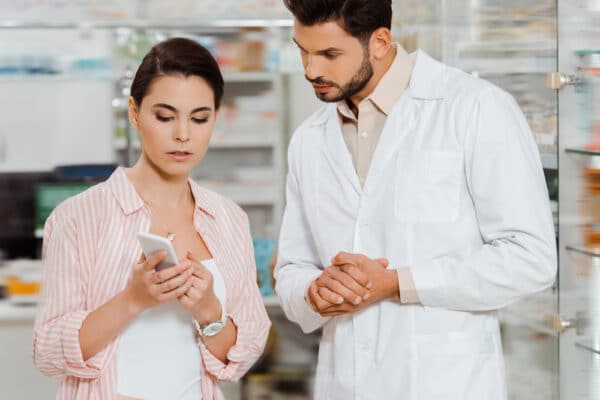 Weibliche Kundin zeigt dem Apotheker das Smartphone als Symbolbild für den Beitrag: E-Rezept