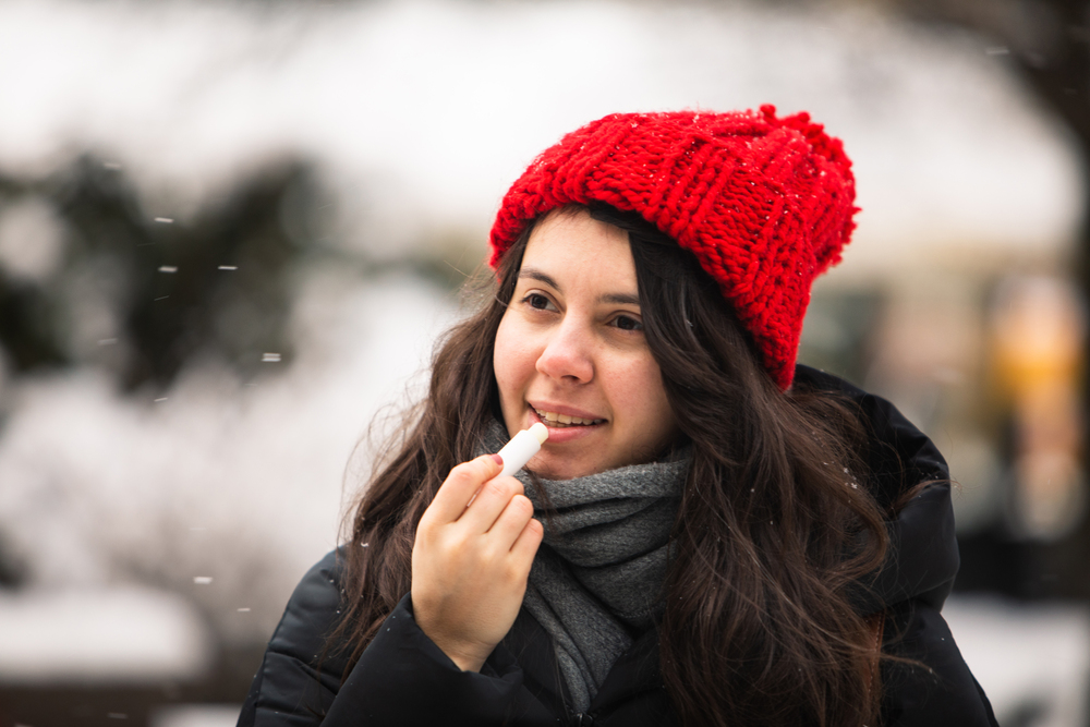 Frau nutzt Lippenpflege bei kaltem Winterwetter als Symbolbild für den Ratgeber: Brennende Lippen im Winter