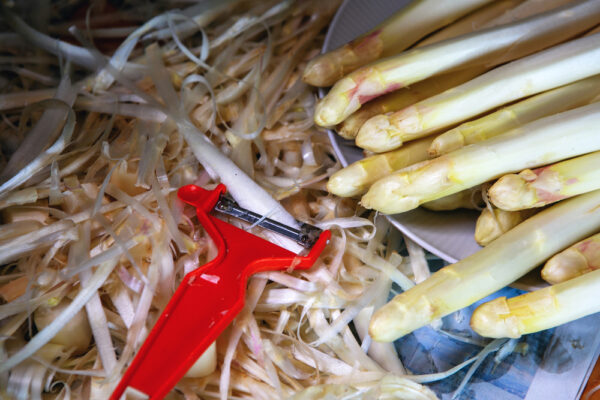 Nahaufnahme von Spargel und seiner Schale und einem roten Messer als Symbolbild für Ratgeber: Spargelsuppe aus Schalen