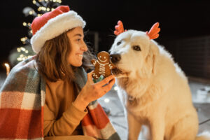 Eine junge Frau füttert ihrem Hund in einer winterlichen Szene Lebkuchen als Symbolbild für den Ratgeber: Dürfen Hunde Lebkuchen essen?