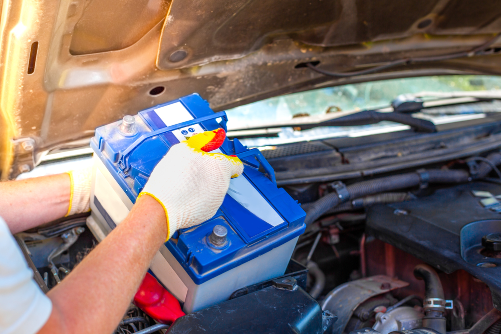 Wartung der Maschine. Ein Automechaniker nimmt eine Batterie unter der Motorhaube eines Autos heraus, um sie zu reparieren, aufzuladen oder zu ersetzen als Symbolbild für Ratgeber: Autobatterie entsorgen