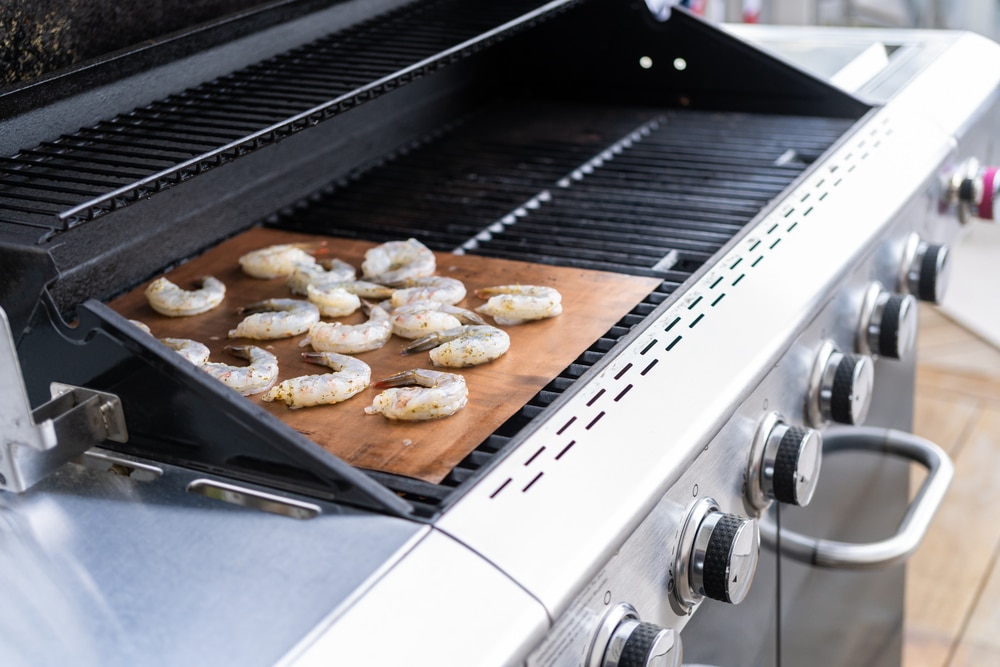 Grillen von Garnelen auf einer Grillmatte über einem Gasgrill im Freien als Symbolbild für den Ratgeber: Alternative zu Alufolie beim Grillen