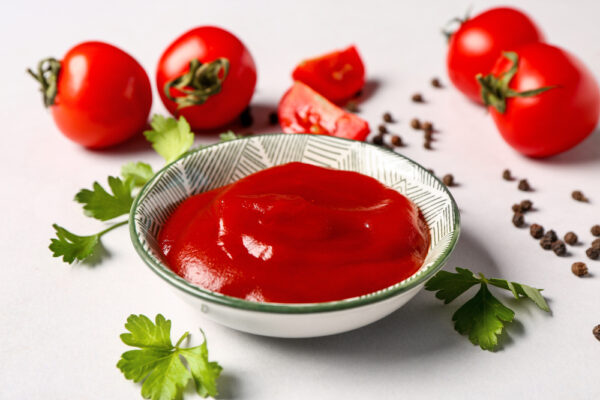 Ein Schälchen voll selbstgemachter Ketchup neben Tomaten und Petersilie