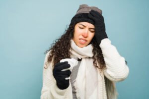 Eine erkältete Frau ist warm eingepackt, sieht geplagt aus und hält sich das Ohr zu als Symbolbild für den Ratgeber: Druck auf den Ohren bei Erkältung