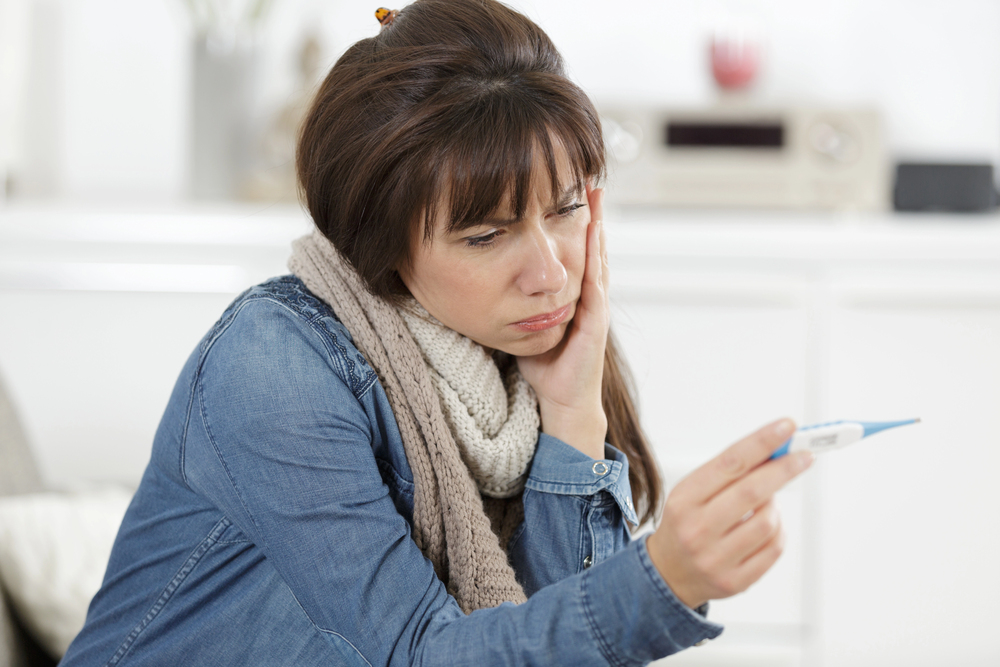 Frau sieht fragend auf ein Fieberthermometer als Symbolbild für den Ratgeber: Ab wann hat man Fieber?