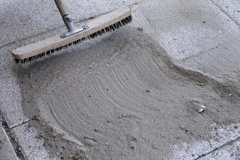 Besen verteilt Fugensand in den Fugen von Pflastersteinen als Symbolbild für den Ratgeber: Fugensand gegen Unkraut