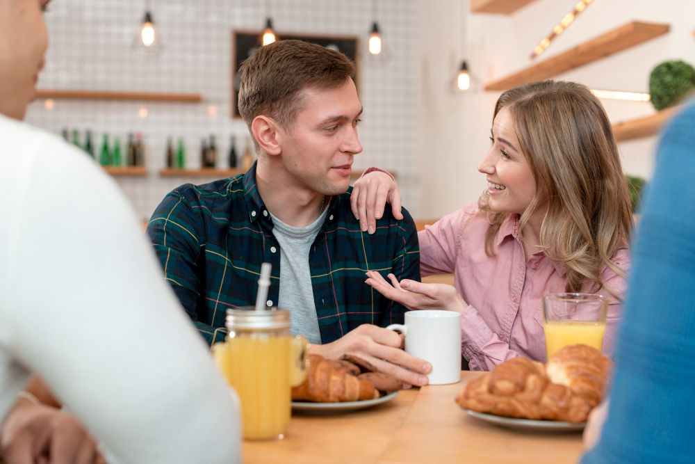 Junges Paar beim Frühstück, die Frau versucht, ihren Freund zu verteidigen. Eltern akzeptieren Freund nicht.