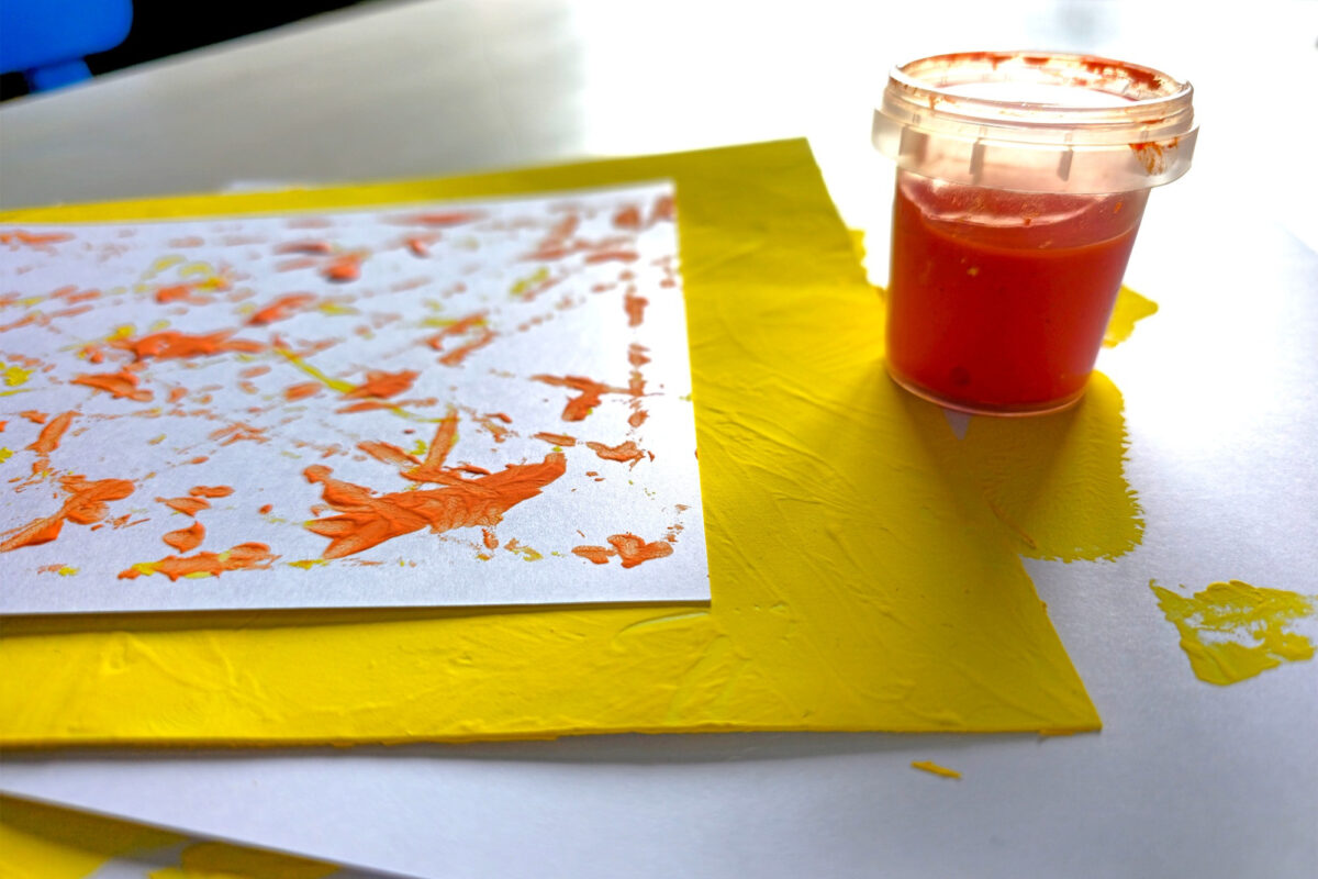Tiegel mit Fingerfarbe in Orange nebst gesammelter "Kunstwerke".