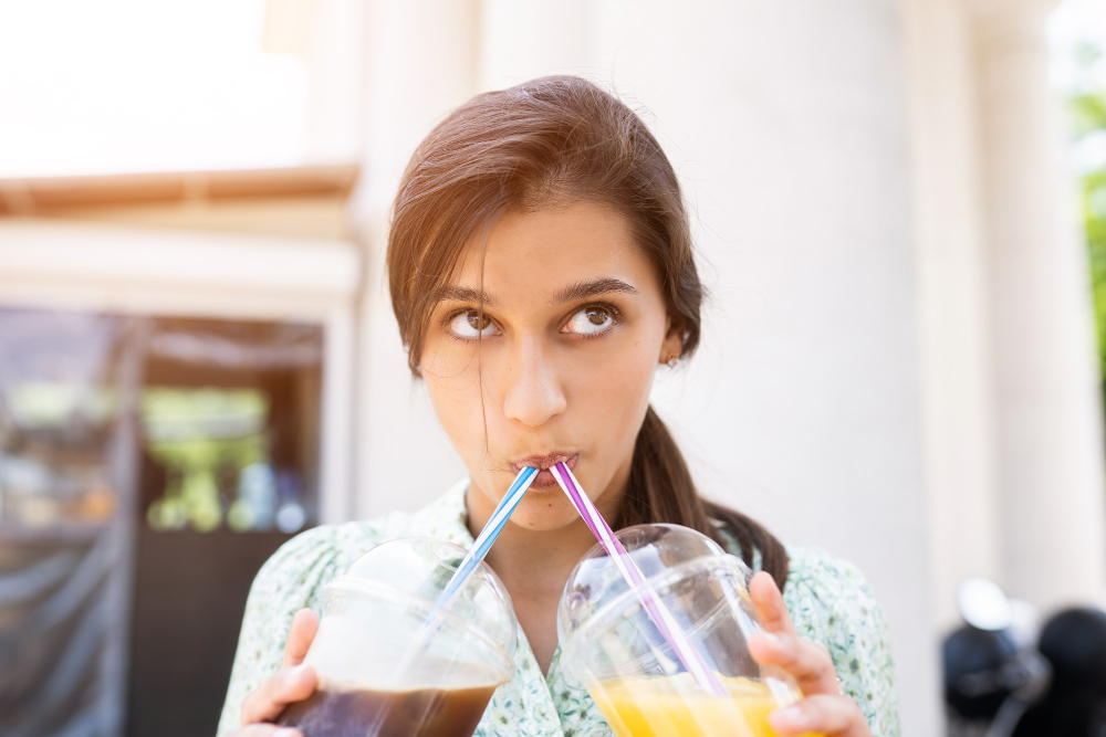 Eine junge Frau trinkt zwei Softdrinks gleichzeitig aus jeweils einem Strohhalm.