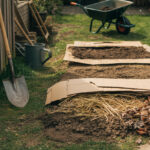 No-Dig-Gartenbeet (ohne Umgraben) mit Karton, Mulch und Werkzeug im Frühling.