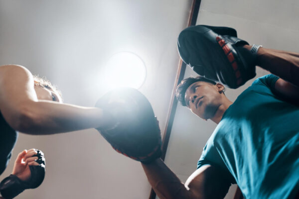 Ein Trainer hält Pratzen, während eine Person Boxbewegungen ausführt. Das Bild zeigt ein Boxtraining und symbolisiert das Thema 'Ist Boxsport schädlich für das Gehirn?' und stellt die körperliche Intensität und potenziellen Risiken von Schlägen im Boxsport dar.