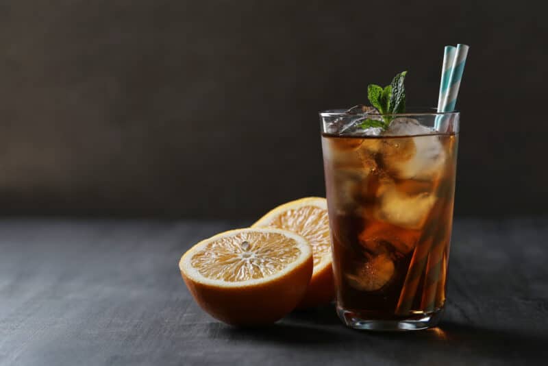 Ein Glas mit Kaffee-Tonic, mit einer Zitrone und Eiswürfeln.