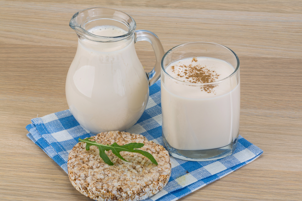 Glas und Kanne mit Buttermilch oder Kefir auf kariertem Tuch, dazu Reiswaffel mit Rucola.