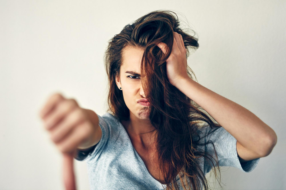 Eine verärgerte Frau hält den Daumen nach unten und greift sich frustriert in die Haare. Das Bild symbolisiert das Thema 'Kleinanzeigen-Verkäufer ändert Preis im Nachhinein' und drückt Ärger und Unzufriedenheit über eine unerwartete Preisänderung bei einem Kauf aus.