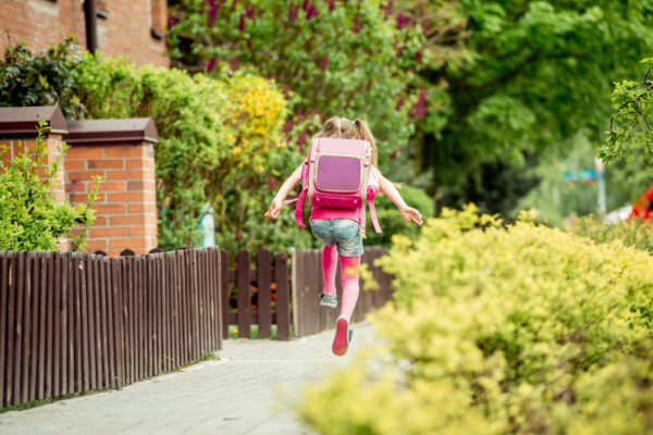 Fröhliches Schulkind mit leichtem Schulranzen springt auf dem Heimweg entlang des Gehwegs.