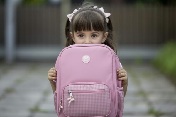Mädchen mit rosa Schleifen im Haar hält einen rosa Schulranzen vor das Gesicht.