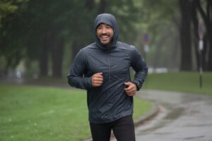 Mann läuft mit Kapuzenjacke bei Regen durch einen Park.