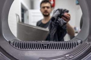 Blick aus dem Inneren eines Trockners auf einen Mann, der Wäsche hineingibt.