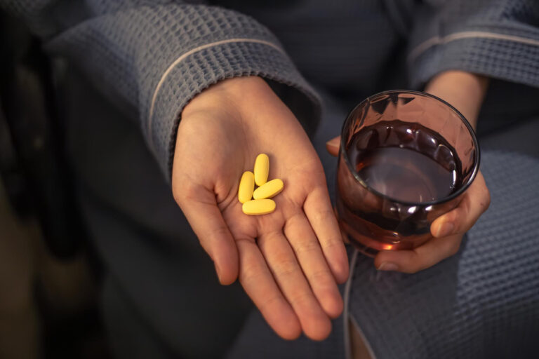 Eine Hand hält mehrere gelbe Tabletten und ein Glas Wasser, passend zur Diskussion über die Risiken, Medikamente auf eigene Faust abzusetzen.
