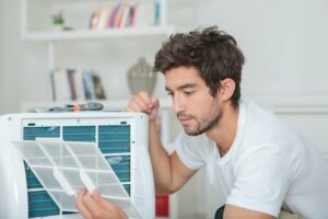 Ein Mann überprüft und reinigt den Filter einer mobilen Klimaanlage – ein wichtiger Schritt beim Desinfizieren der mobilen Klimaanlage.