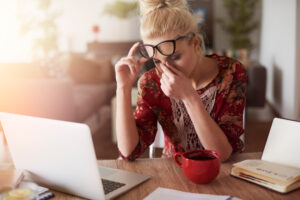 Müde Frau am Nachmittag im Homeoffice mit Laptop und Kaffee