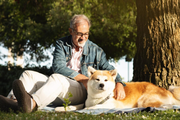 Alter Mann sitzt auf einer Decke mit einem Hund (Akita)