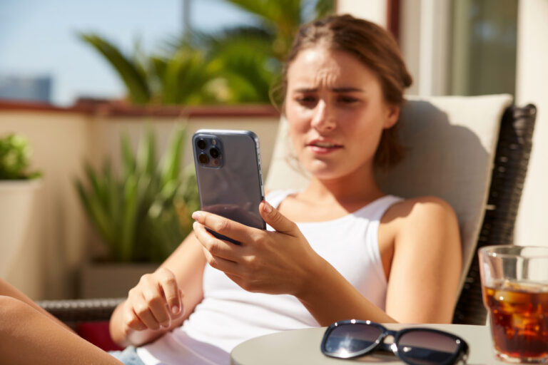 Frau im Sonnenschein blickt besorgt auf ihr Smartphone.