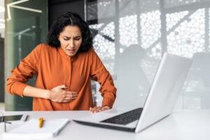 Eine Frau sitzt am Arbeitsplatz und hält sich den Bauch als Symbolbild für Sodbrennen durch Stress
