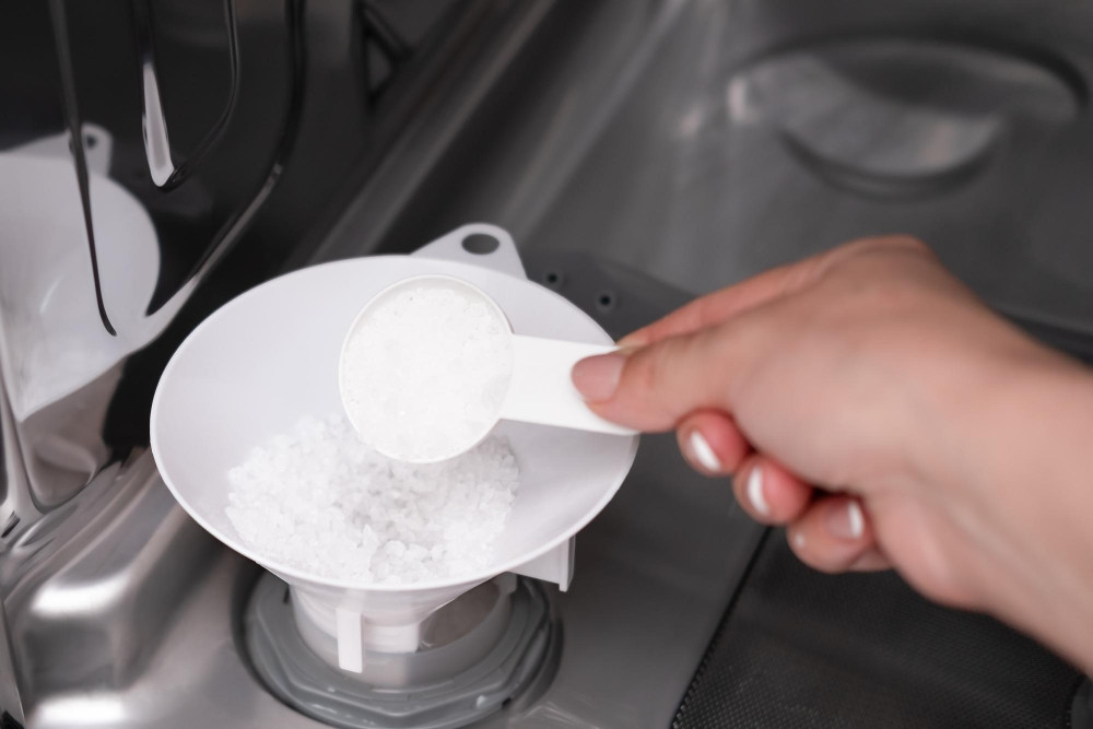Frau füllt Spülmaschinensalz über einen Trichter in die Öffnung für Spülmaschinensalz in den Geschirrspüler ein.