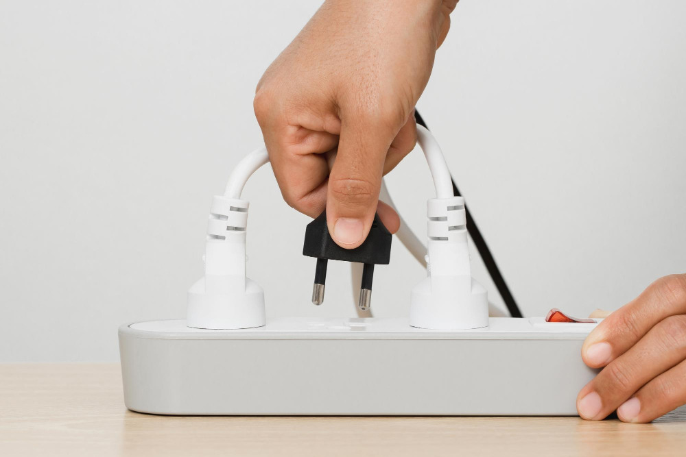 Hand steckt den Stecker eines Haushaltsgeräts in die Steckdosenleiste